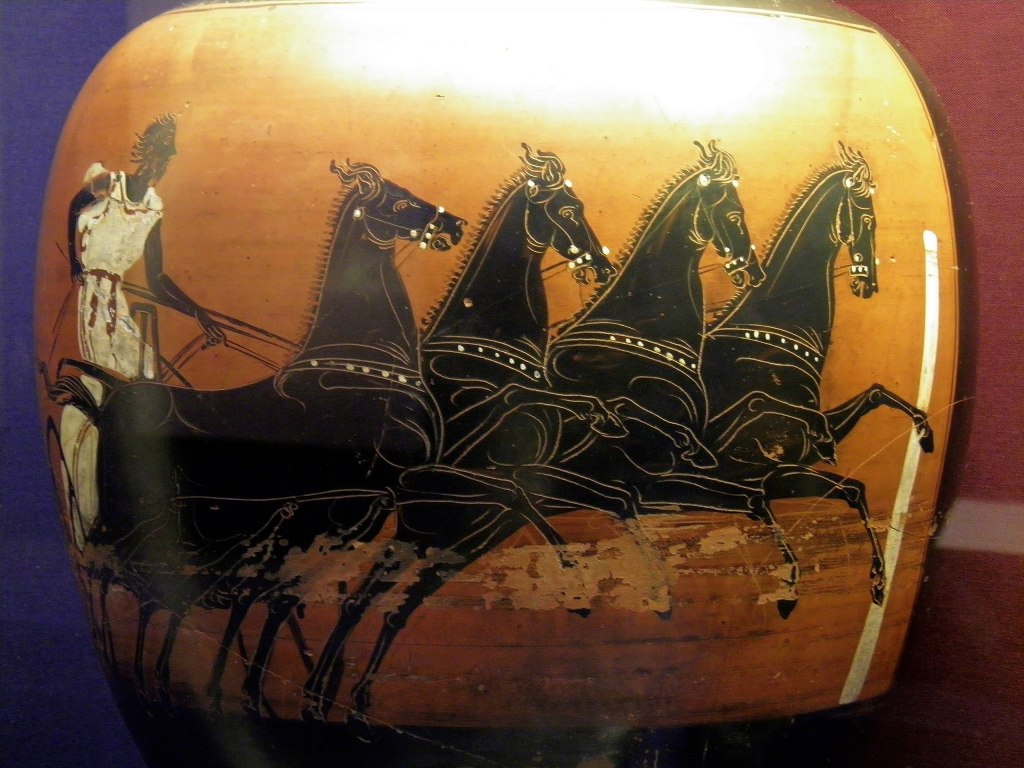 Description from Wikimedia Commons: "This vase belongs to a distinctive type given as a prize to the winner of the chariot race in the ancient games held at Athens during the yearly festival known as the Panathenaia. The festival honoured Athena, the city's patron deity. The vase would have been one of 140, each containing 40 litres of olive oil, given to the winner. Chariot racing was the most popular spectator sport in ancient times. Up to 40 chariots could compete in a race and crashes were common. The two turning posts at either end of the oblong course were the most dangerous parts of the track. The painter of this vase has been highly successful in creating the illusion of speed as the chariot careers along. A quadriga chariot drawn by four horses is shown, the hair and tunic of the charioteer are blown back, and the manes and tails of the horses fly in the rush of air. The chariot is coming up to a post which may represent the turn or the finish of the race. Both moments would be climaxes. While the sport for which the prize was given was shown on one side of these vessels, Athena herself was usually shown on the other side. On this one she wears a high-crested helmet, an elaborately decorated chiton (tunic), and her characteristic aegis, a snake-fringed poncho worn around her neck."